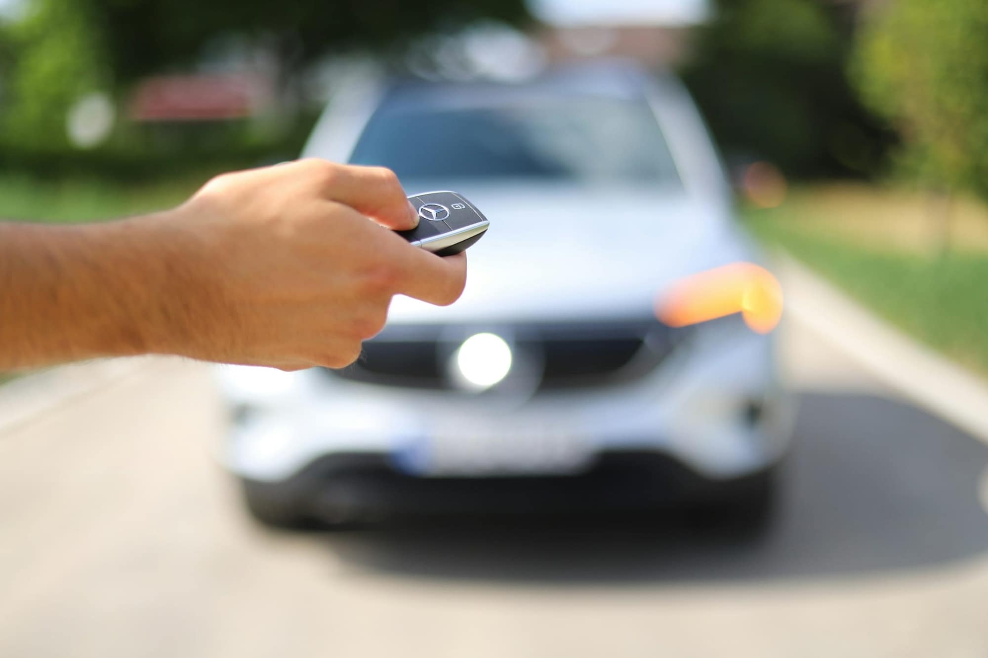 Une main ouvre une voiture avec la clé, sur une route ensoleillée