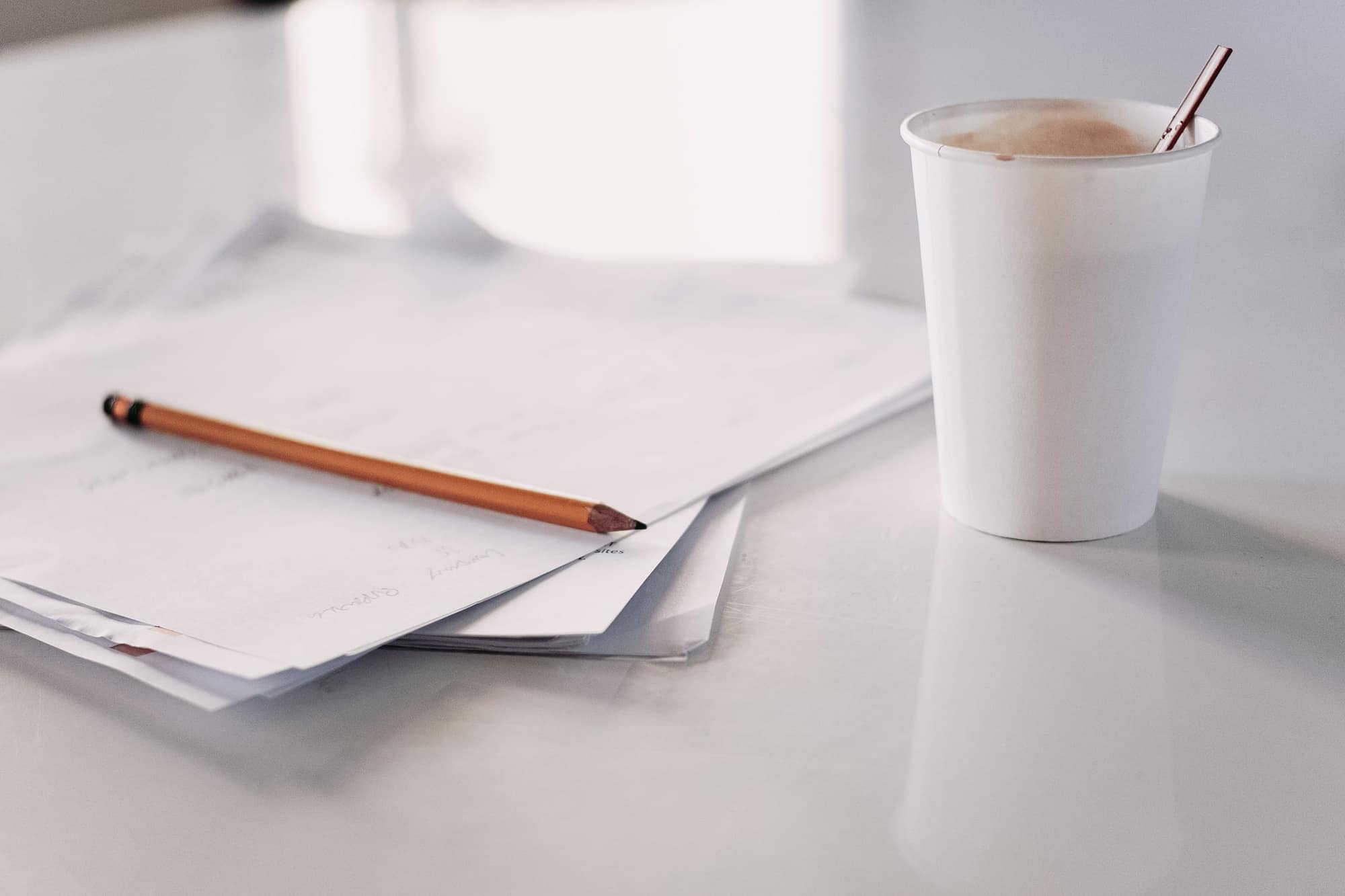 Des papiers, un crayon et un café sur une table blanche